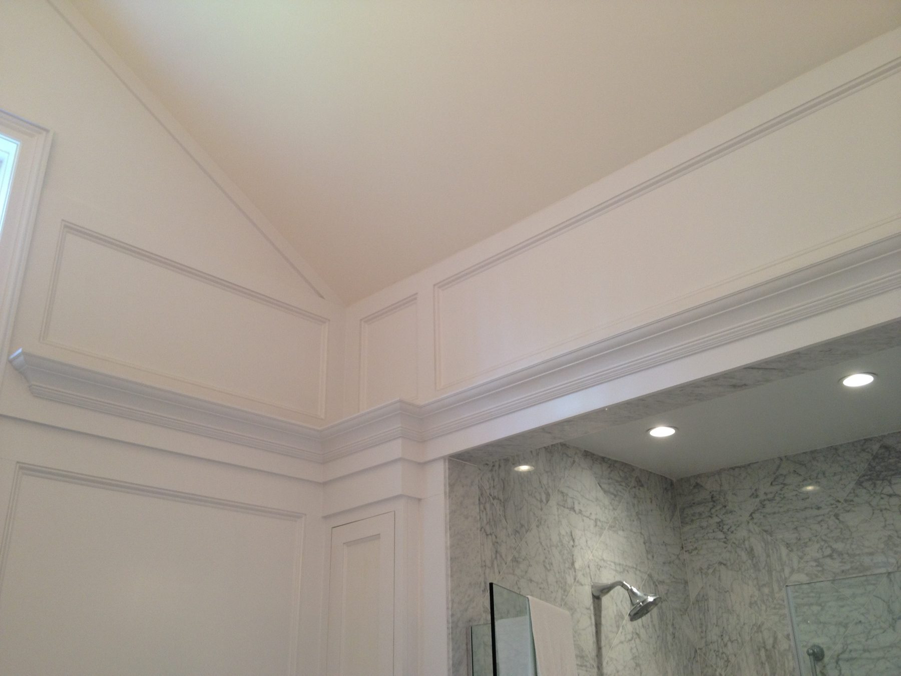 Layered crown molding, applied wall paneling, and a vaulted ceiling detail in a bathroom finished by Leslie Guerci
